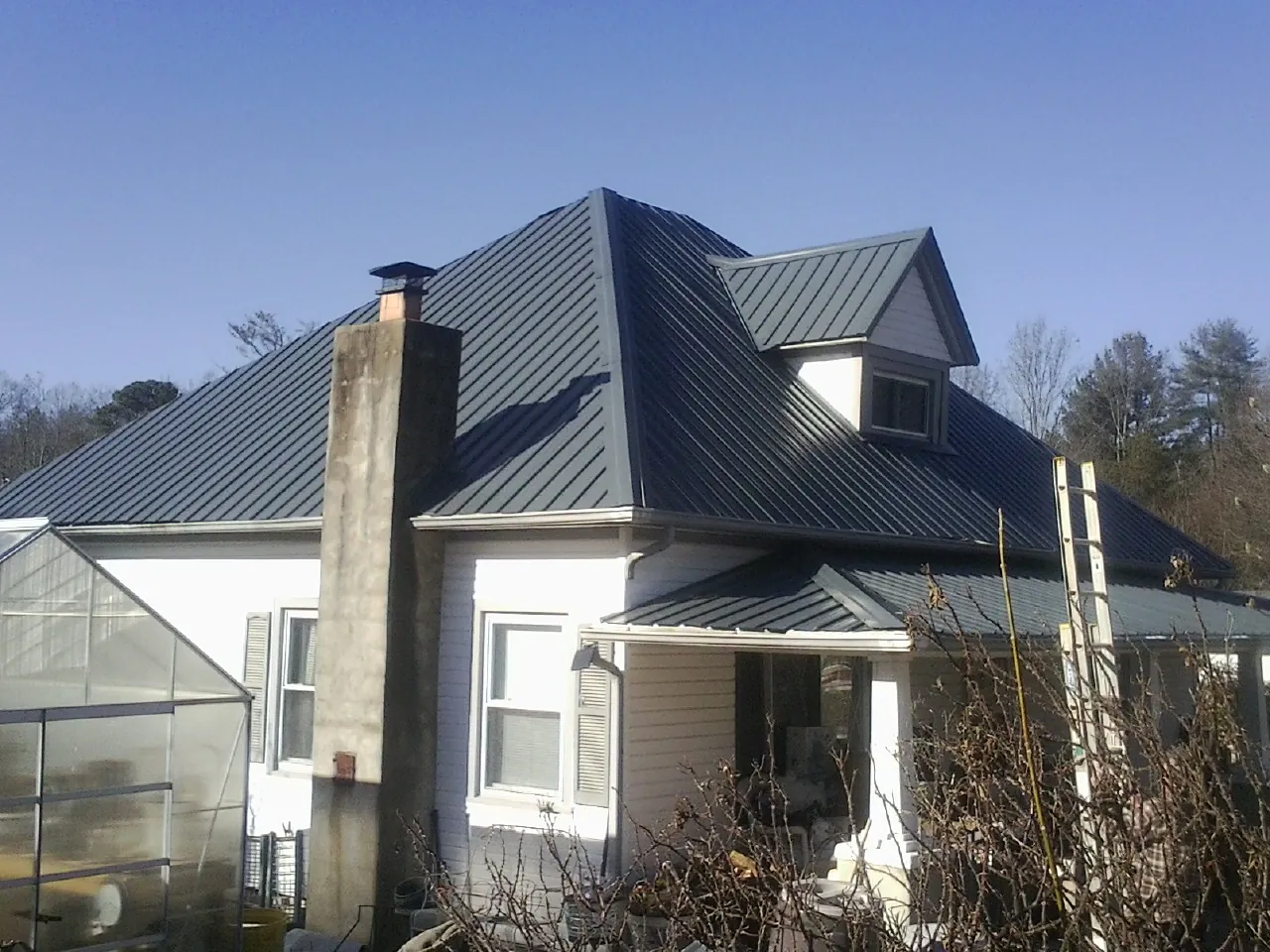 Dark blue standing seam metal roof on a white farmhouse with dormer — Slate & Tile Roof Repair by Roofing Brothers in North Charleston