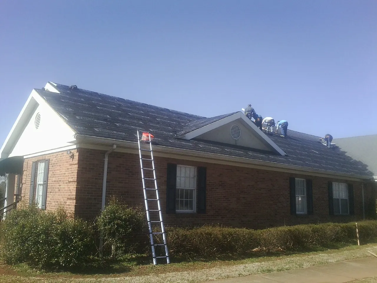 Crew tearing shingles off a brick ranch roof with a ladder set — Emergency Roof Repair work by our crew in North Charleston