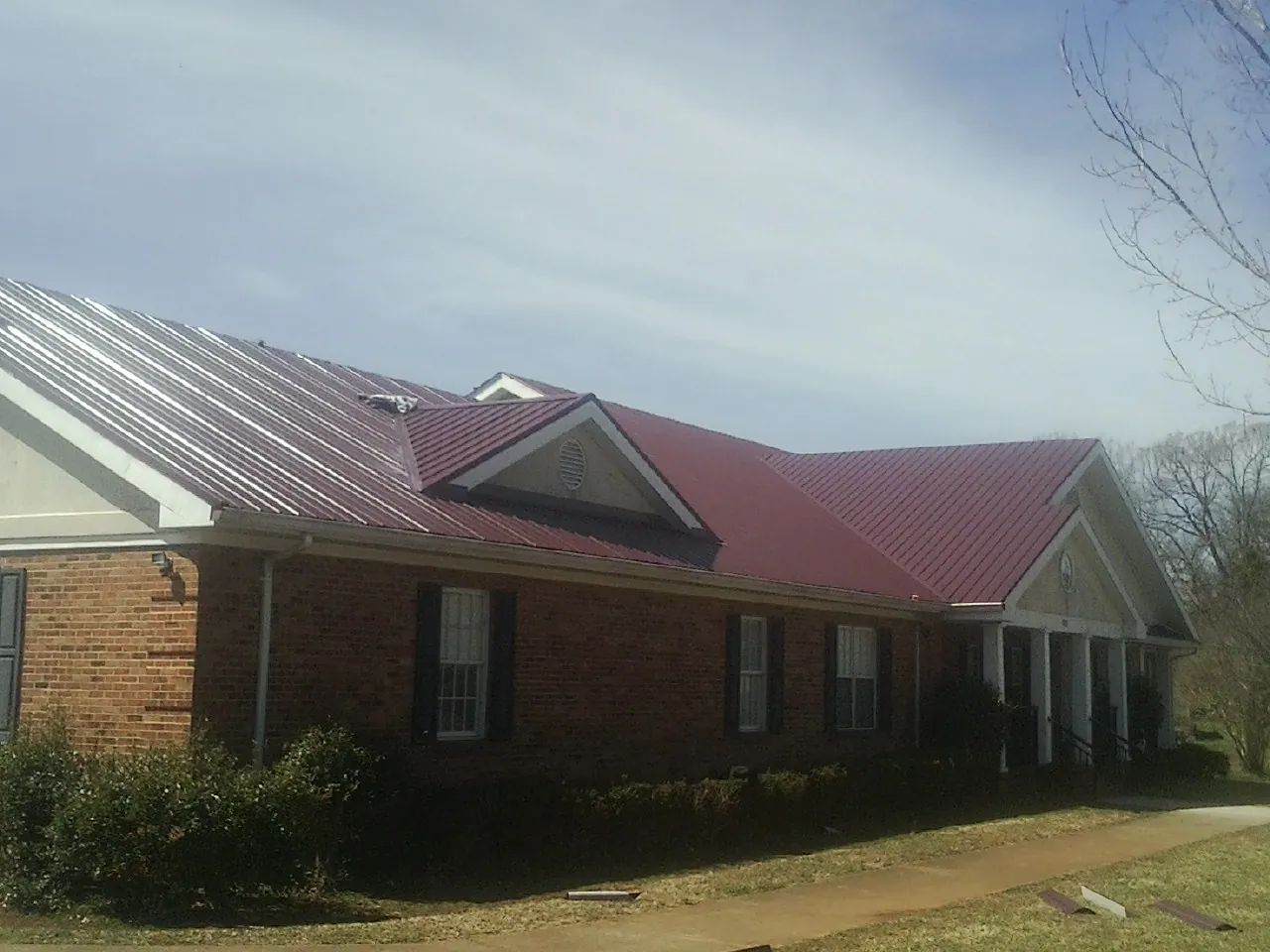 Red metal roof with gabled entries on a long brick building, from a Hail Damage Roof Repair job in North Charleston