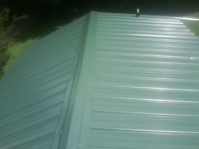 New green metal panels meeting at the ridge of a roof — Flat Roof Repair work by our crew in North Charleston