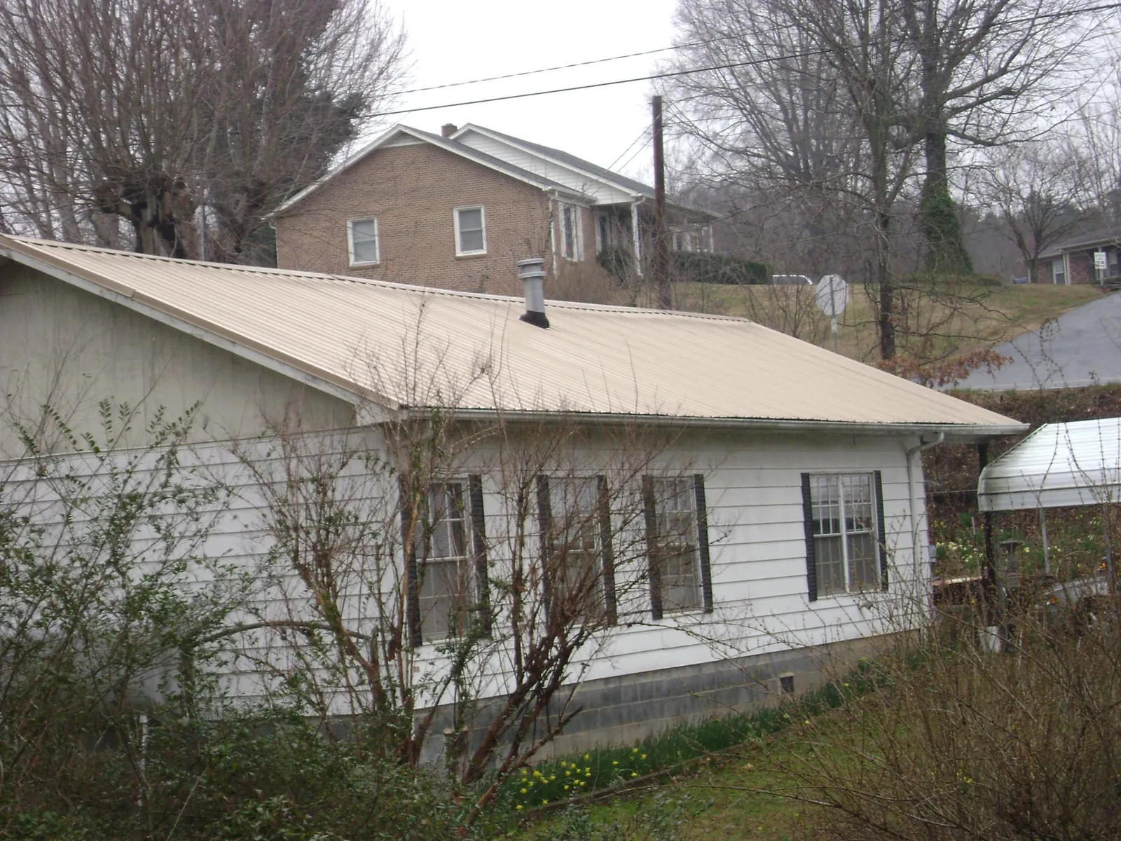 Tan metal roof on a white sided house set into a hillside — Commercial Roofing by Roofing Brothers in North Charleston